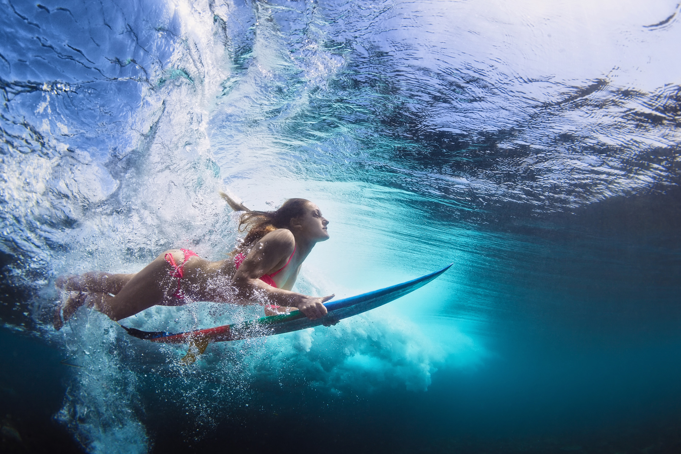 Frau taucht mit Surfbrett unter Wasser