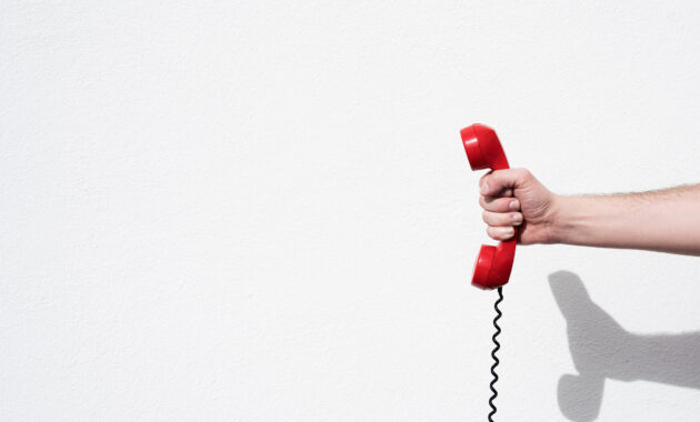 hand mit rotem kabeltelefon vor weißer wand