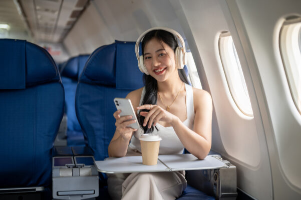flugzeug frau mit kopfhörern und handy lächelt ins bild